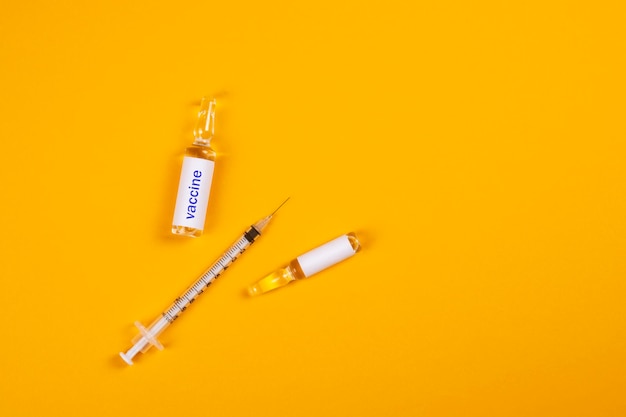 Het concept van bescherming tegen het COVID-19-virus. Spuit en ampul met een vaccin op een gele achtergrond.