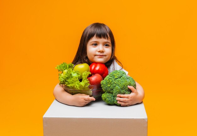 Het concept van biologisch voedsel klein meisje met een mand met fruit en groenten op een gele achtergrond Gezonde babyvoeding