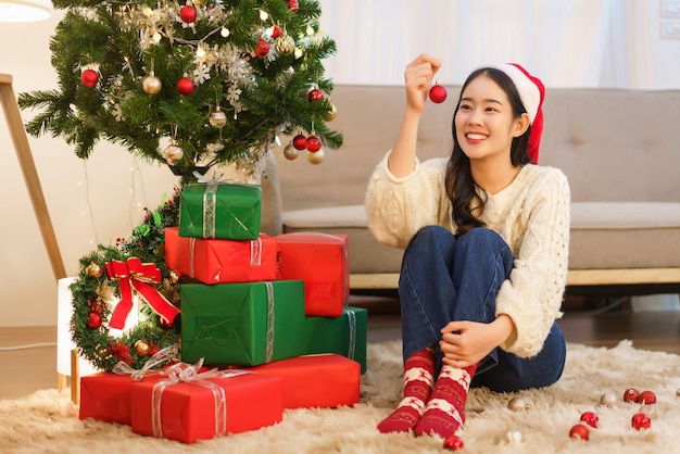 Het concept van de viering van Kerstmis Jonge Aziatische vrouw die rode bal houdt om in kerstboom te verfraaien