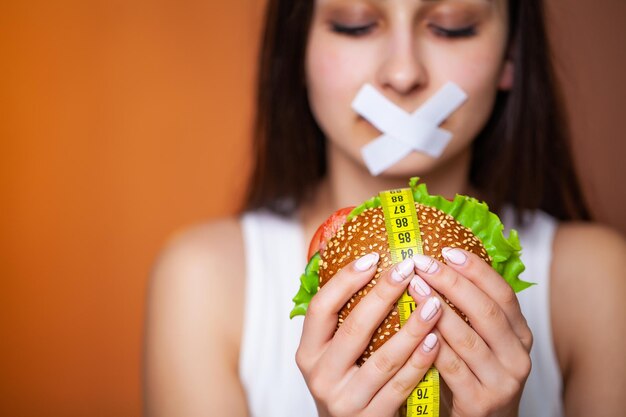 Het concept van een dieetvrouw met verzegelde mond houdt een vette hamburger.