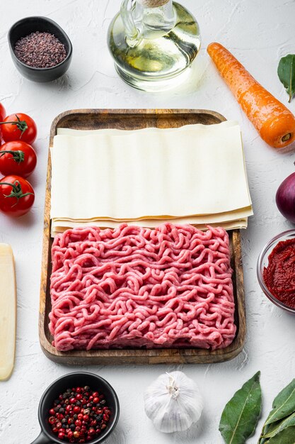 Het concept van het koken van lasagne. ingrediënten, lasagnebladen, basilicum, kerstomaatjes, parmezaanse kaas, knoflook, paprikareeks, op witte stenen tafel