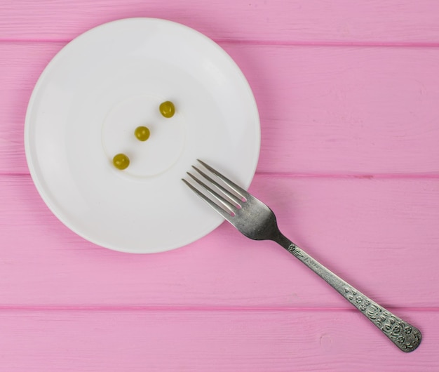 Het concept van honger boulimia Een paar erwten op een witte plaat en een vork