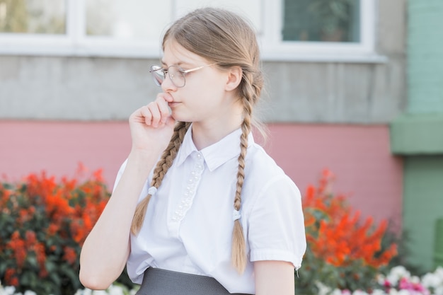 Het concept van onderwijs. Meisje leerling van de basisschool in glazen in uniform. Nadenkend meisje in glazen klaar voor school.