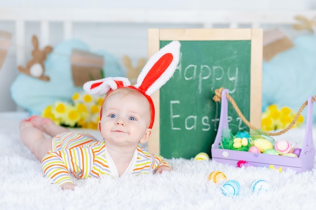 Het concept van Pasen, een baby in een konijnenhoed op een bed met paaseieren en de inscriptie vrolijk Pasen