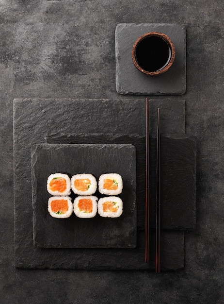 Het concept van sushi-maki met zalmkomkommer en nori op zwarte leistenen planken met sojasaus Traditioneel Japans eten Bovenaanzicht