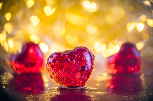 Het concept van Valentijnsdag, liefde. drie rode glazen harten in druppels water tegen de achtergrond van de lichten. zoek naar liefde, zoek naar je soulmate