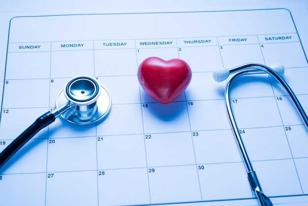 Foto het controleren van uw hartconcept close-up foto van het bovenaanzicht van de werkplek van de dokter met kalender medisch hulpmiddel en klein rood hart