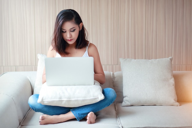 Het de vrouwenportret van Beautyful die computer met wit vest en blauw Jean in woonkamer met behulp van ontspant dag