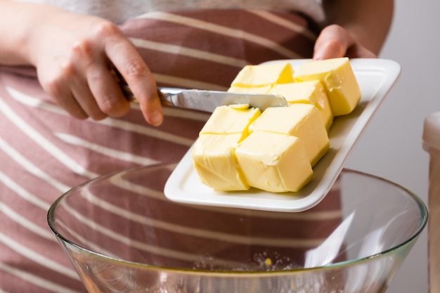 Het deegbereidingsproces vrouwelijke handen voegen boter toe aan de mengkom voor het bakken van cake op een zwarte...