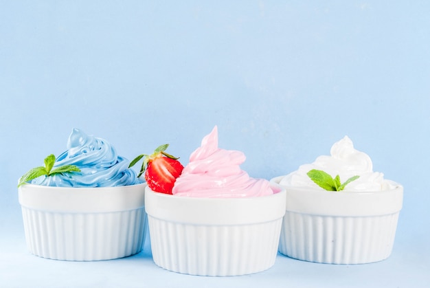Het dessert van de gezonde voedingzomer, vanille en bessen bevroren yoghurt of zacht roomijs in witte kommen, dat op lichtblauwe achtergrond wordt geïsoleerd