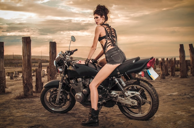 Het donkerbruine meisje in zwarte leerlaarzen en denimborrels zit op een motorfiets