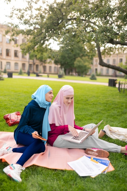 Het dragen van heldere hijaabs. Aantrekkelijke studenten met heldere hijabs die zich vrolijk voelen terwijl ze samen buiten studeren