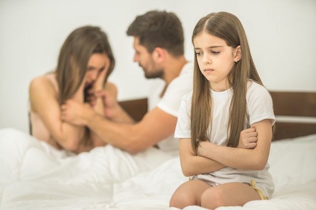 Het droevige meisje dat bij de ouders op het bed zit