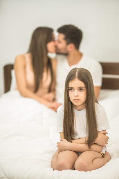 Het droevige meisje zit bij de kussende ouders op het bed