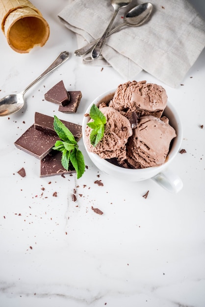 Het eigengemaakte chocoladeroomijs diende met verse munt, donkere chocolade en wafelroomijskegels, witte marmeren achtergrondexemplaar ruimte hoogste mening