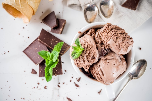 Het eigengemaakte chocoladeroomijs diende met verse munt, donkere chocolade en wafelroomijskegels, witte marmeren achtergrondexemplaar ruimte hoogste mening