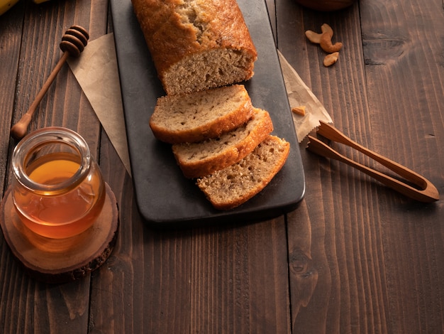 Het eigengemaakte die pond van het banaanbrood met cashewnoten en honing op houten lijst wordt gesneden.