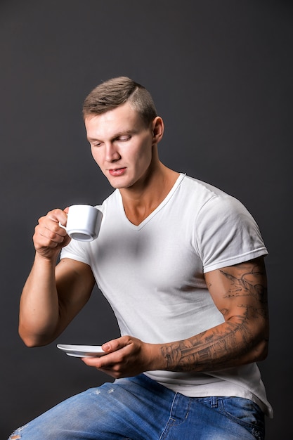 Het elegante atletische mens glimlachen, die koffiekop houden. Zitten.