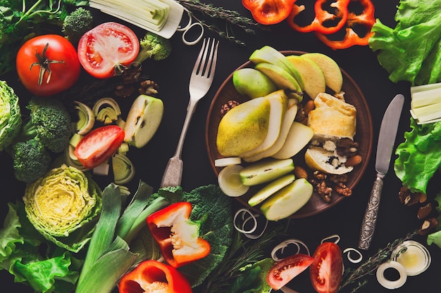 Het eten van gezond plantaardig voedsel op zwarte achtergrond. Verse biologische paprika's, tomaat, kool en andere maaltijden met lege plaat, kopieer ruimte