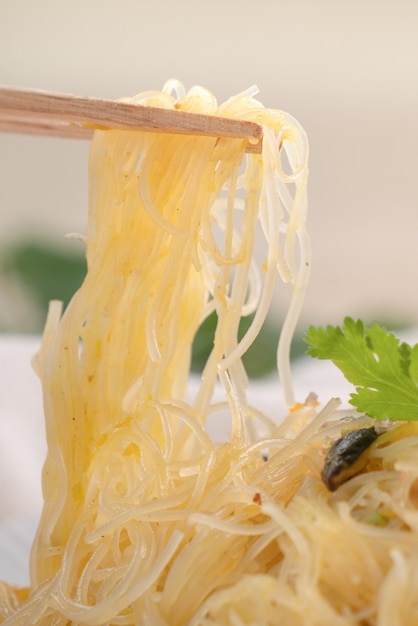 Het eten van rijst vermicelli noedels geroerbakt met gekookte pompoen en groenten op houten tafel oppervlak.