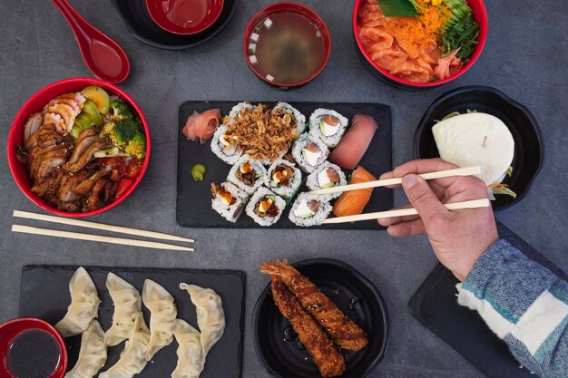 Het eten van sushi rolt Japans eten restaurant geassorteerde sushi schotel Close-up van de hand met rollende eetstokjes met rustieke achtergrond