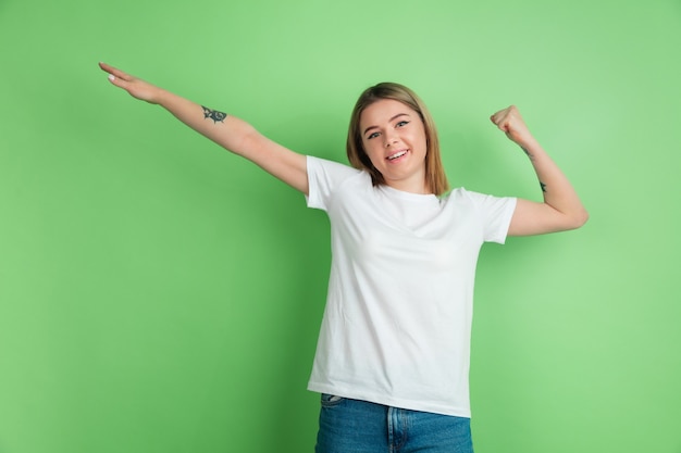 Het gebaar van de winnaar. Het portret van de blanke jonge vrouw op de groene studiomuur