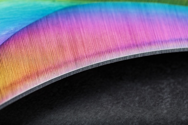 Foto het gebogen scherpe lemmet van de kerambit dagger is een gradiënt regenboogkleur op een donkere achtergrond. koud staal, close-up