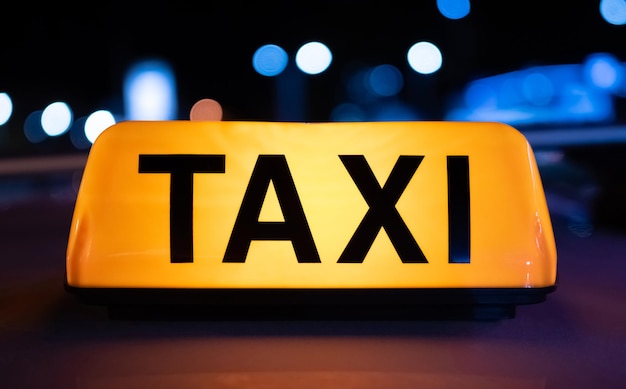 Het gele lichtteken van de taxiauto op donkere straat bij nacht met de dienstsymbool van de verlichtingscabine met neon gl