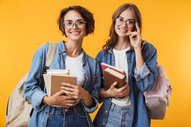 Het gelukkige emotionele jonge vrouwenvrienden stellen geïsoleerd over de gele boeken van de muurholding.