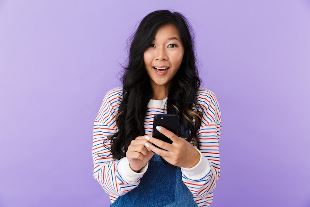 Het gelukkige jonge Aziatische mooie aantrekkelijke vrouw stellen geïsoleerd binnen met behulp van mobiele telefoon