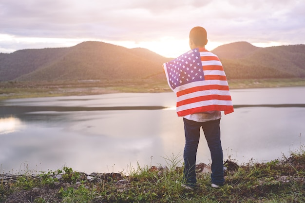 Het gelukkige jonge geitje met een hande hield Amerikaanse vlag in de de zomerzonneschijn. 4 juli - onafhankelijkheid