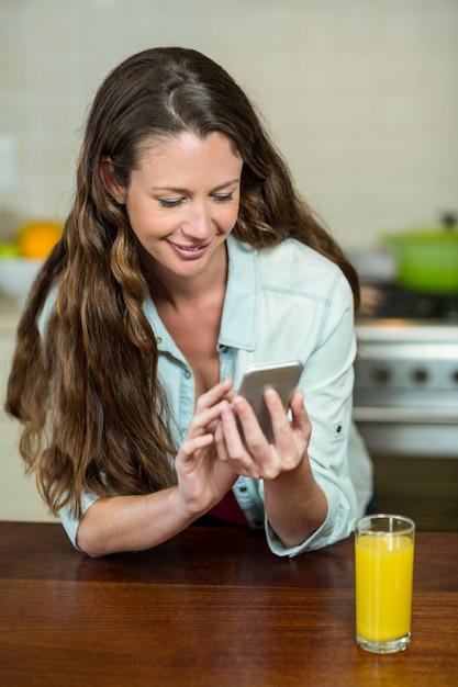 Het gelukkige jonge overseinen van de vrouwentekst op mobiele telefoon in keuken