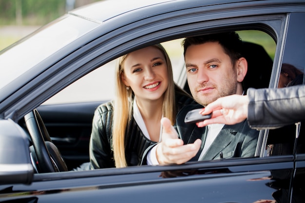 Het gelukkige jonge paar kiest en koopt een nieuwe auto voor het gezin