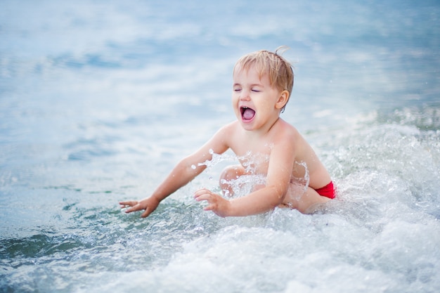 Het gelukkige jongen spelen bij ondiep watergolf