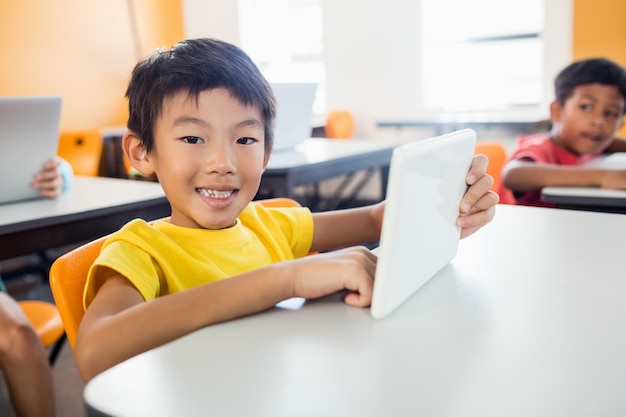 Het gelukkige jongen stellen met tablet bij bureau