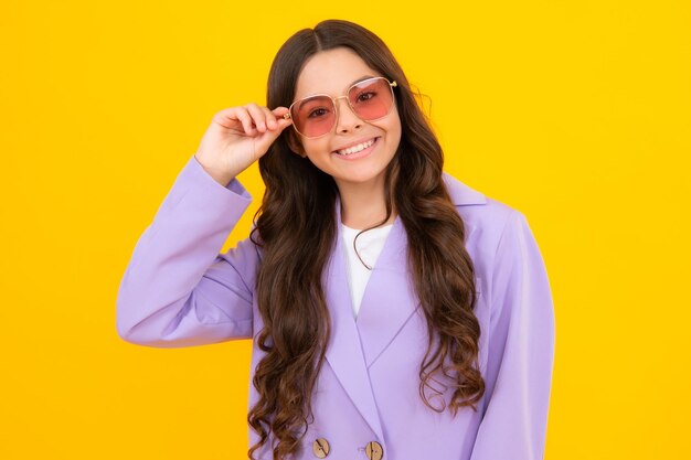 Het gelukkige meisje die van het tienerkind zonnebril op gele studioachtergrond dragen meisje in glazen