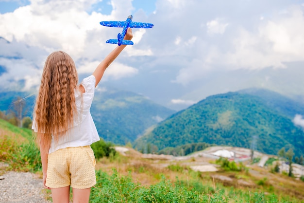 Het gelukkige meisje met stuk speelgoed vliegtuig dient binnen bergen in
