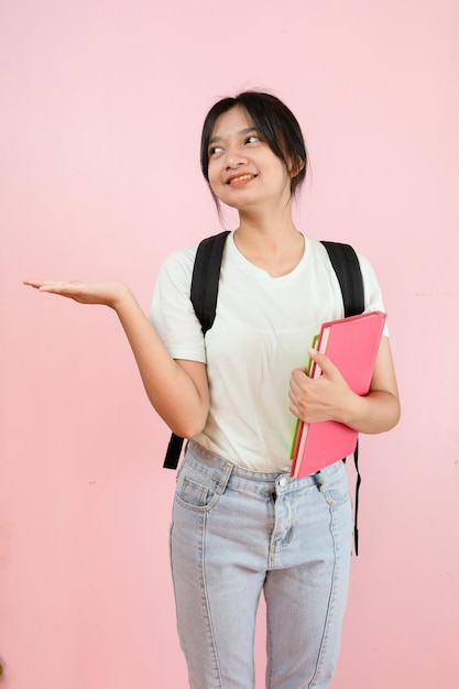 Het gelukkige studenten jonge meisje houdt roze boek en rugzak op roze achtergrond