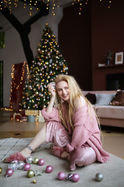 Het gelukkige vrolijke blonde vrouw stellen door de kerstboom