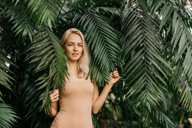 Het gezicht van de jonge vrouw omringd door tropische bladeren. Close-upportret van prachtige dame met natuurlijke naakte make-up, perfecte huid, blond haar. Natuurlijke cosmetica, wellness, zuiverheid, huidverzorging, schoonheidsconcept