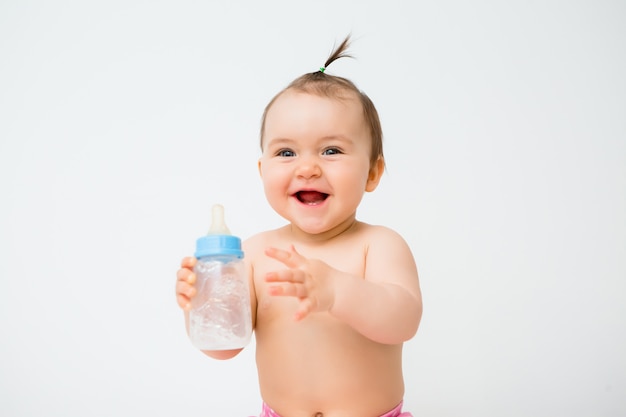 Het gezonde babymeisje glimlacht en houdt een waterfles