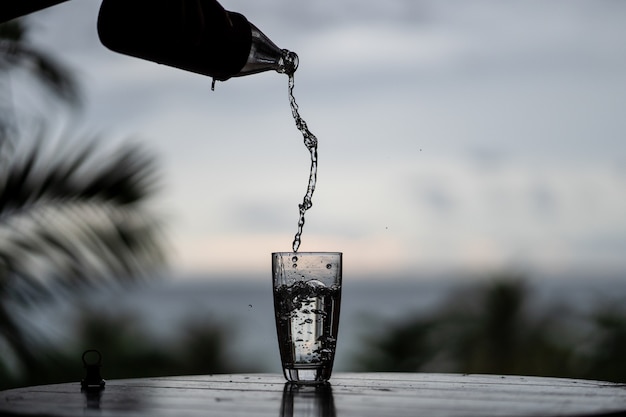 Het gieten van water uit de fles in het glas op aardachtergrond