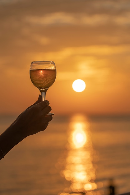 Foto het glas van de handholding wijn tegen een mooie zonsondergang dichtbij overzees op het tropische strand