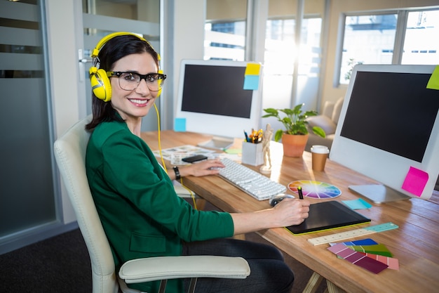 Het glimlachen brunette die bij haar bureau en het luisteren muziek werken