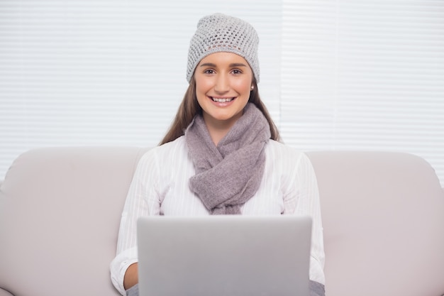 Het glimlachen brunette met de winterhoed bij het gebruiken van haar laptop