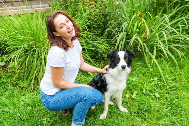 Het glimlachen het jonge aantrekkelijke vrouw spelen met leuke puppyhond border collie in de zomertuin of stadspark. Meisje training truc met hond vriend. Dierenverzorging en dieren concept.