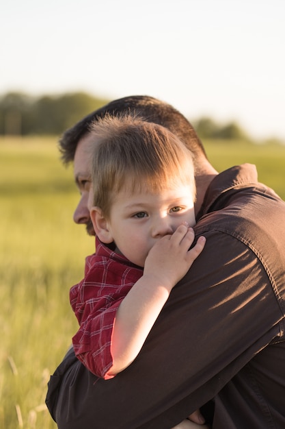 Foto het glimlachen het jonge papa en zoonsomhelzing ontspannen bij weide.