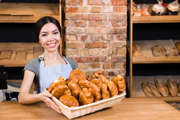 Het glimlachen portret van een jonge vrouw die verse gebakken croissantmand in de bakkerijwinkel houden