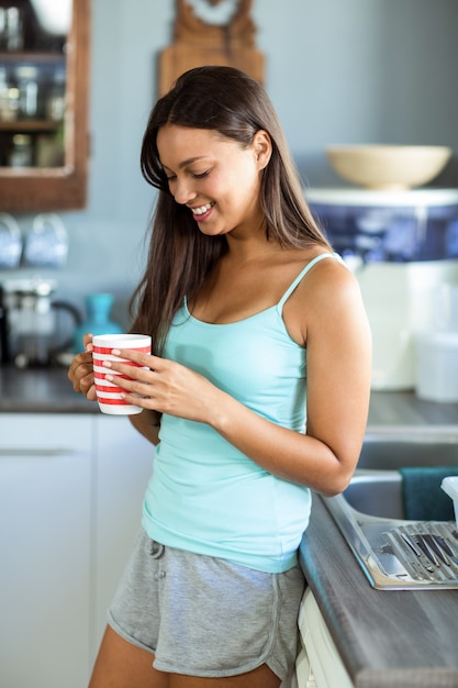 Het glimlachen van de koffiekop van de vrouwenholding in keuken