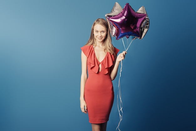 Het glimlachen van jonge de sterballons van de meisjesholding op blauwe muur